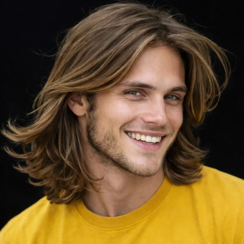 Man with long, wavy hair and a French crop fade, wearing a yellow t-shirt and smiling confidently. Stylish and modern long hairstyle for men, offering a carefree, natural look.