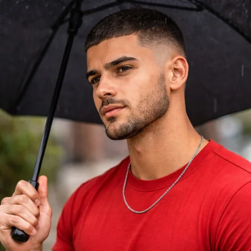 Buzz cut french crop mid fade on young Arabic man wearing red shirt and holding umbrella showing ultra short top and clean mid fade modern athletic mens hairstyle
